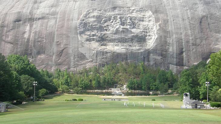 A large stone mountain with a carving on it and trees and grass in front of it A large stone mountain with a carving on it and trees and grass in front of it