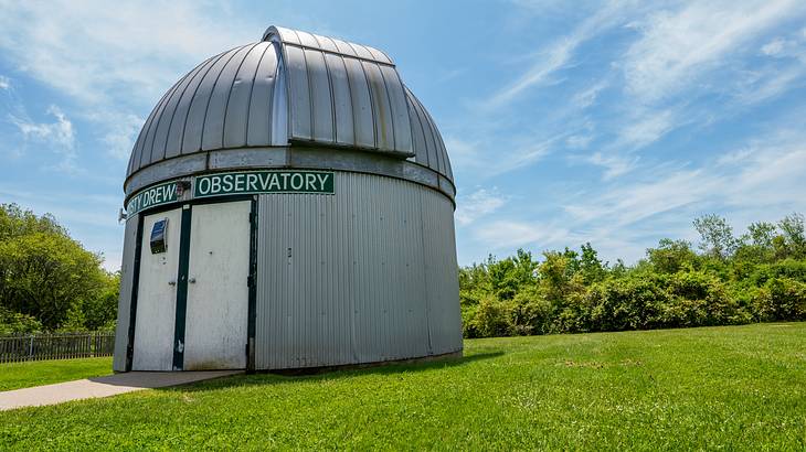 A silver-grey domed building with an observatory sign sitting on the grass A silver-grey domed building with an observatory sign sitting on the grass