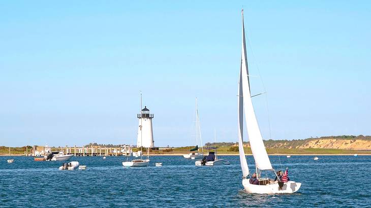 A sailboat on the water with a lighthouse and small cliffs in the distance
