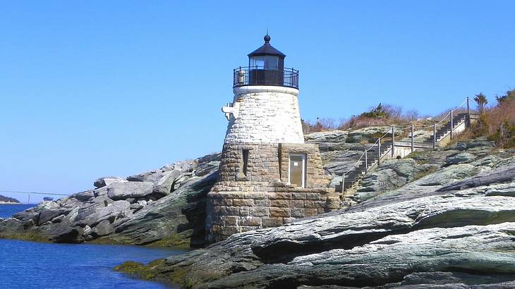 A small lighthouse sitting on the rocks with ocean water to the side A small lighthouse sitting on the rocks with ocean water to the side