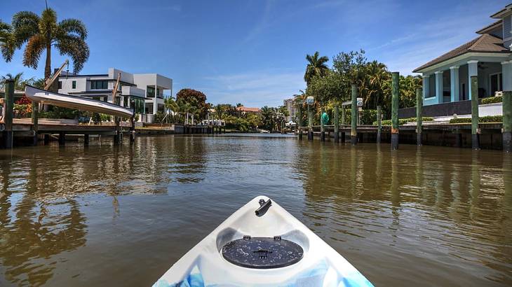 Looking towards the tip of a kayak on a lake with wooden docks and palm trees around
