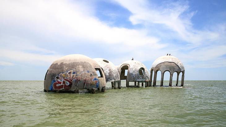 Four greyish dome structures, one with some graffiti, on the sea