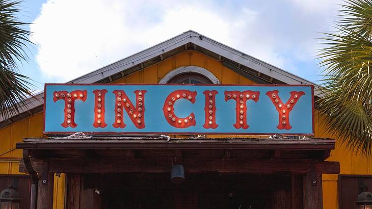 A vernacular yellow structure with a blue board saying "Tin City" in red font color
