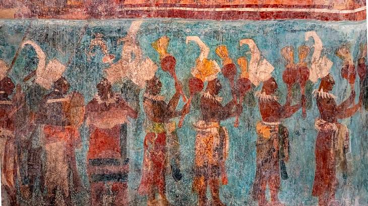 An ancient mural on a partly blue wall showing Mayans standing in a line