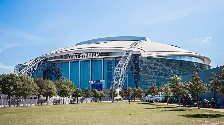 A football stadium that says "AT&T Stadium" with grass and trees in front of it A football stadium that says "AT&T Stadium" with grass and trees in front of it