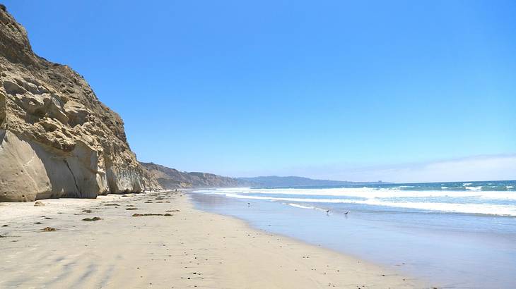 A white sand beach with a cliff to one side and ocean waves crashing on to the shore