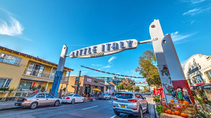 A sign that says "Little Italy" on a street with cars and a market display