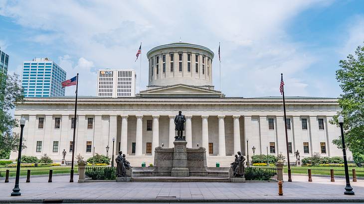 A white stone building a statue, a path, and flags in front of it