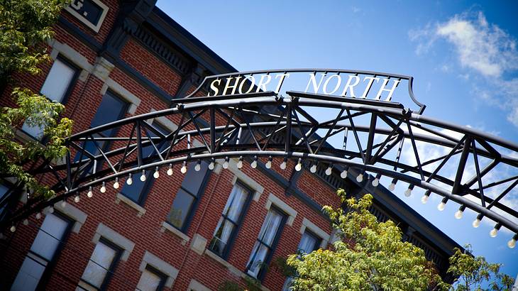 An iron sign that says "Short North" with a red brick building and trees behind it