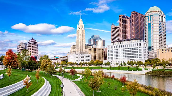 A path with grass on either side and a river and city skyline on the right-hand side