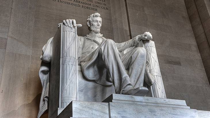 A statue of Abraham Lincoln sitting on a chair with a stone wall behind it