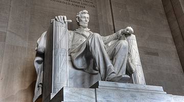 A statue of Abraham Lincoln sitting on a chair with a stone wall behind it