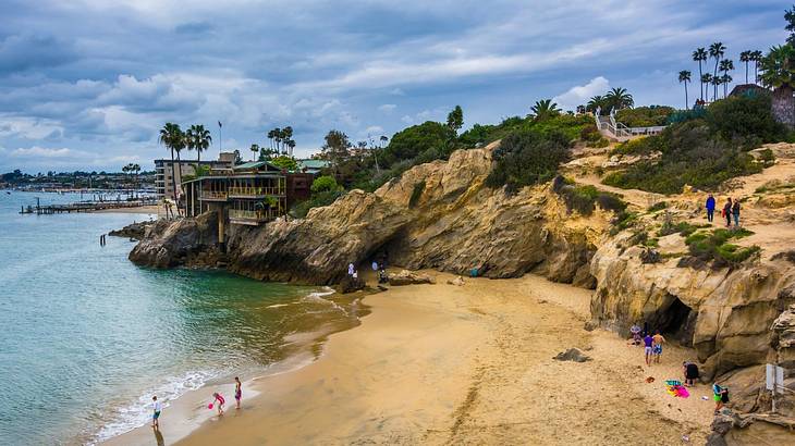 Aerial of a beach with a small cove and a cliff with bushes under a cloudy sky