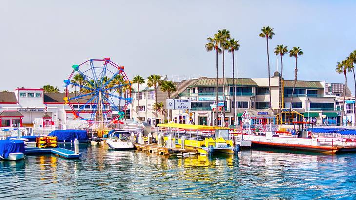 Multi-colored boats moored to a pier against white buildings and a Ferris wheel