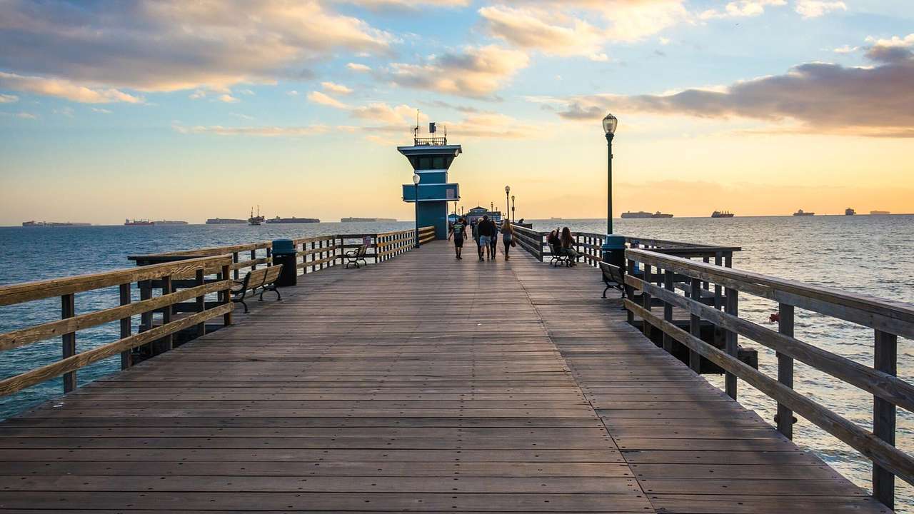 A boardwalk over water with benches, against a partly cloudy sunset sky