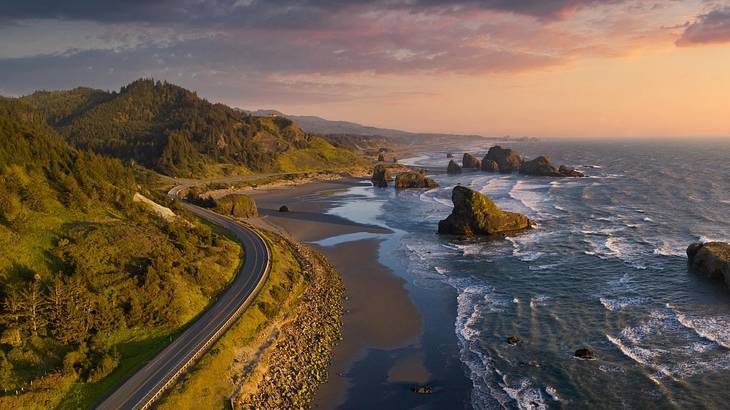 Aerial of a road winding around a green cliff with a shoreline on the side