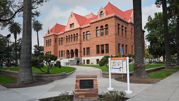 A pathway between green grass to a Romanesque Revival brown building with a red roof