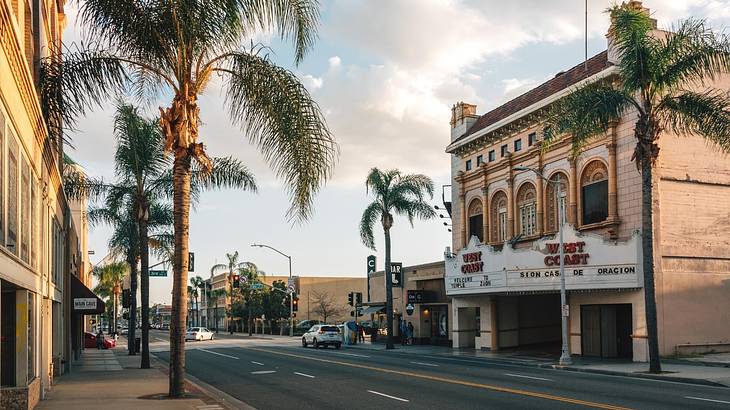 A street with buildings and palm trees on each side, under a partly cloudy sky