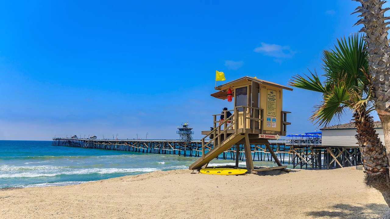 Looking towards a beach with a lifeguard tower and a pier over water under a blue sky