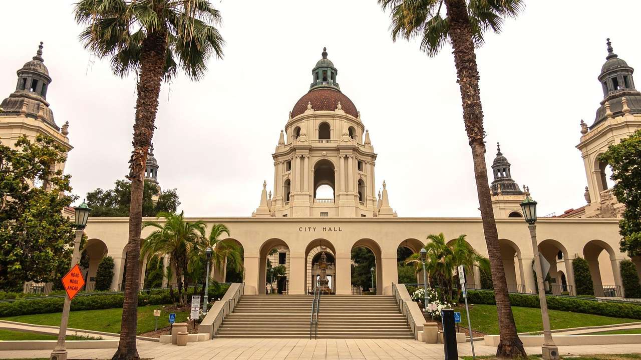 A city hall building with arches and a brown dome, surrounded by green grass