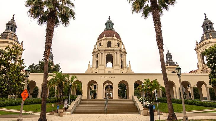 A city hall building with arches and a brown dome, surrounded by green grass