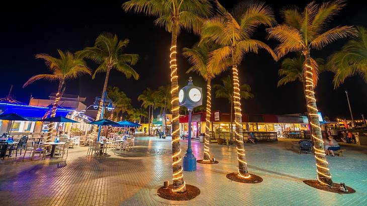 Illuminated fairy lights wrapped around palm trees in front of lit-up outdoor dining