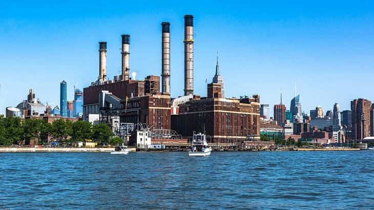Powerplant with tall chimneys, trees, white boats and skyscrapers from across water