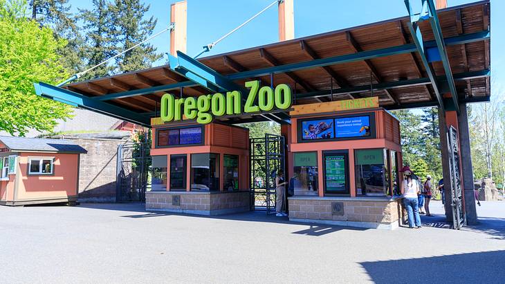 An entrance with two ticket booths and a green sign "Oregon Zoo" on a sunny day