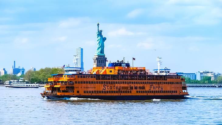 An orange ferry on the water with the Statue of Liberty behind it