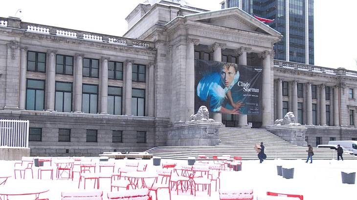 A Greek-style museum building with a banner on it and snow and chairs in front of it