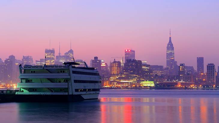 A cruise boat on the water with a skyline in the background and pink sky