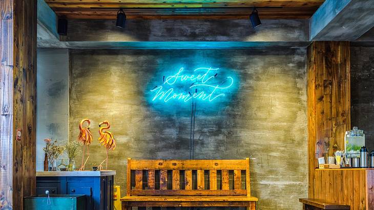 A bench in front of a wall with a blue neon sign that says "Sweet Moment"