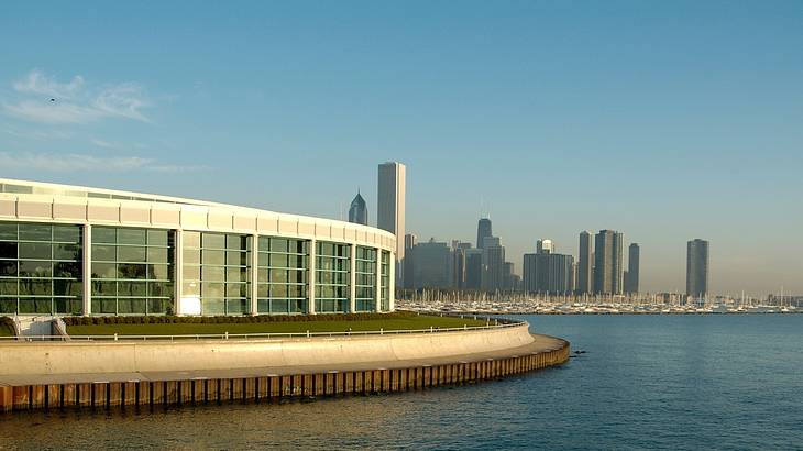 A building with glass windows by the water with a city skyline in the background