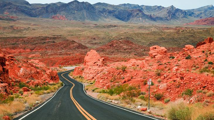 A road winding through red rocks with a mountain range in the distance