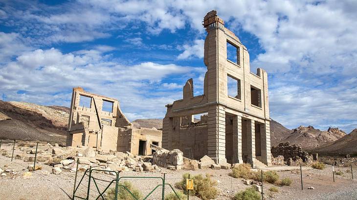 Ruins of a building in a desert landscape under a blue sky with clouds