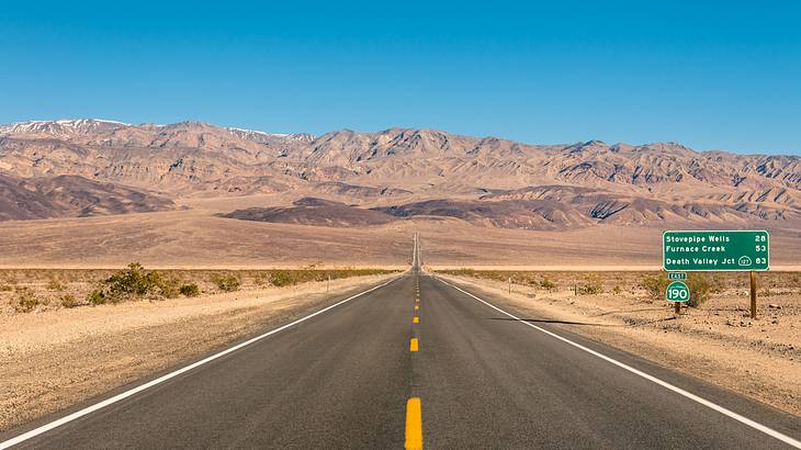 A road leading to sand-colored mountains with desert on either side
