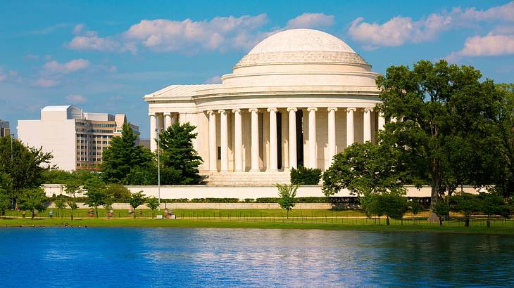 Neoclassical dome-shaped structure with trees around on a lawn facing the water Neoclassical dome-shaped structure with trees around on a lawn facing the water