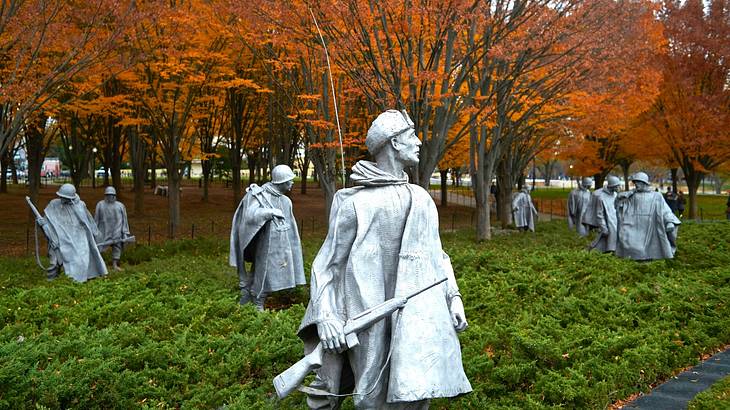 Stainless steel soldier statues among green bushes and golden leafy trees