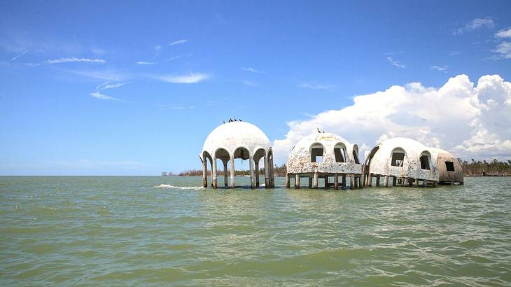 White hut-like structures in the ocean under a blue sky with clouds
