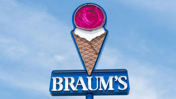 Looking up at a pink ice cream cone sign titled "BRAUM'S" against blue sky