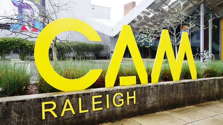 A yellow sign that says "CAM Raleigh" with a path and garden around it