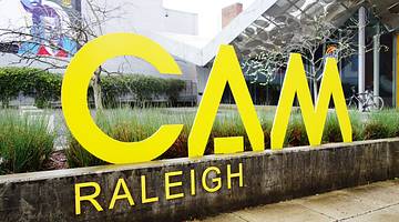 A yellow sign that says "CAM Raleigh" with a path and garden around it