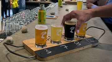 A person picking up a beer from a flight of four beers on a bar