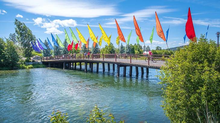 A pedestrian bridge over water with multi-color flags under a partly cloudy sky