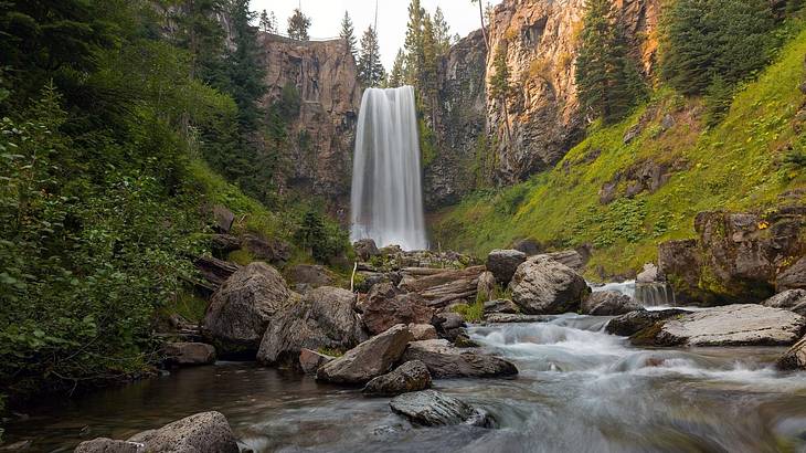 Shallow water with some rocks against a waterfall surrounded by cliffs with greenery