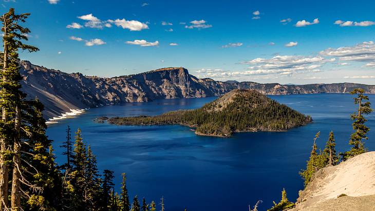 Cliffs surrounding a blue lake with a hill in the middle under a partly cloudy sky