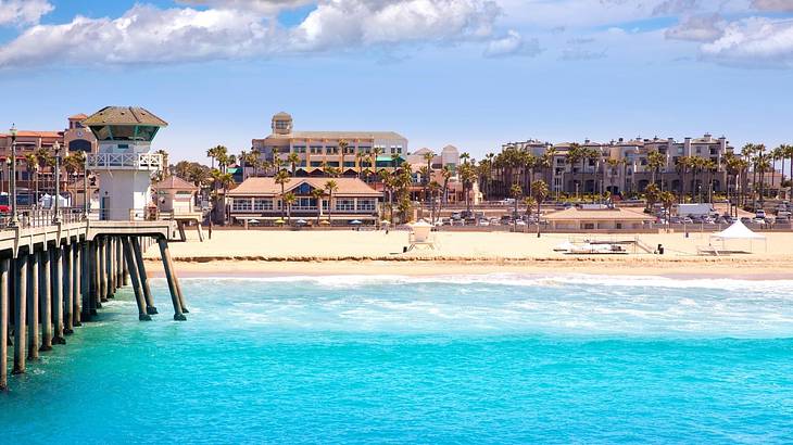 Bright blue water, a sandy shore, and a pier, with buildings in the background Bright blue water, a sandy shore, and a pier, with buildings in the background