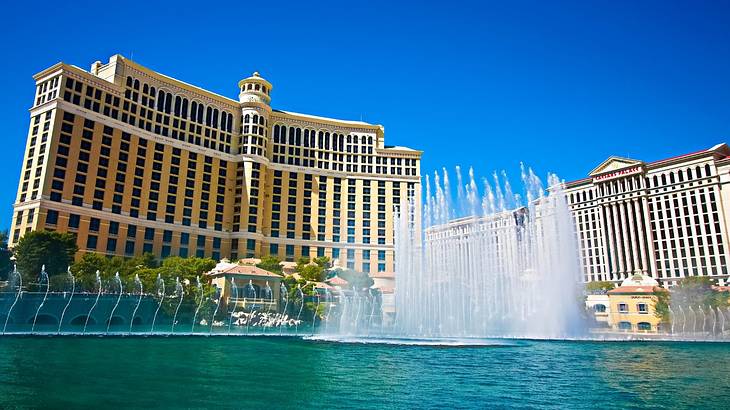 Fountains spraying out of a pond in front of a regal hotel with a blue sky above