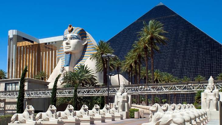 A Sphinx statue and glass pyramid next to a gold building under a blue sky
