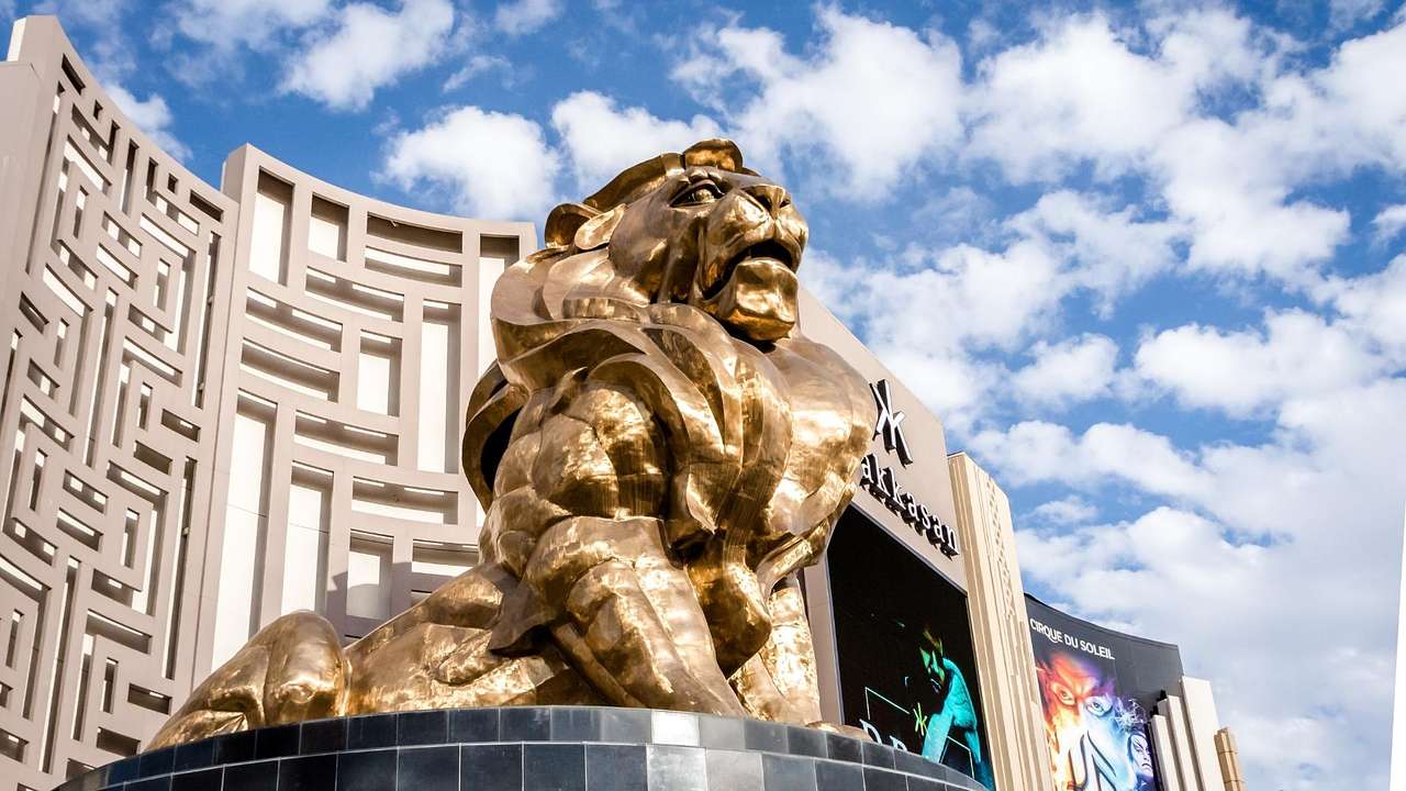 A bronze lion statue with a patterned wall behind it under a partly cloudy sky